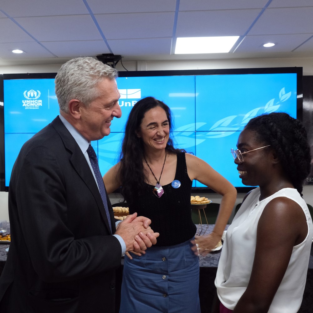 Alto Comissário Filippo Grandi em encontro com as universidades conveniadas à Cátedra Sérgio Vieira de Mello A imagem mostra três pessoas conversando em frente a uma grande tela que exibe o logotipo e o texto do ACNUR (Alto Comissariado das Nações Unidas para Refugiados).