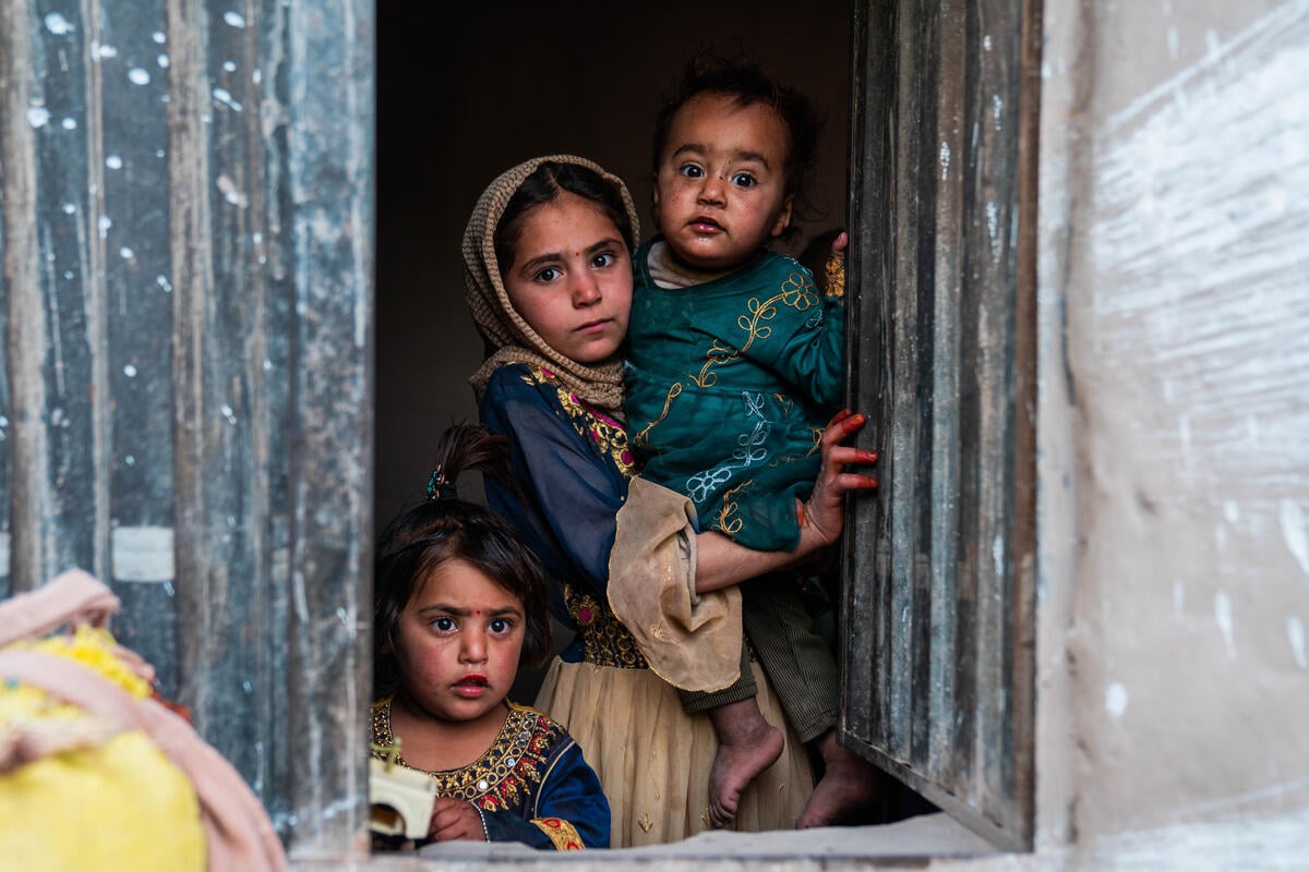 Dos niñas y un niño de distintas edades se asoman por una ventana; sus rostros muestran preocupación.