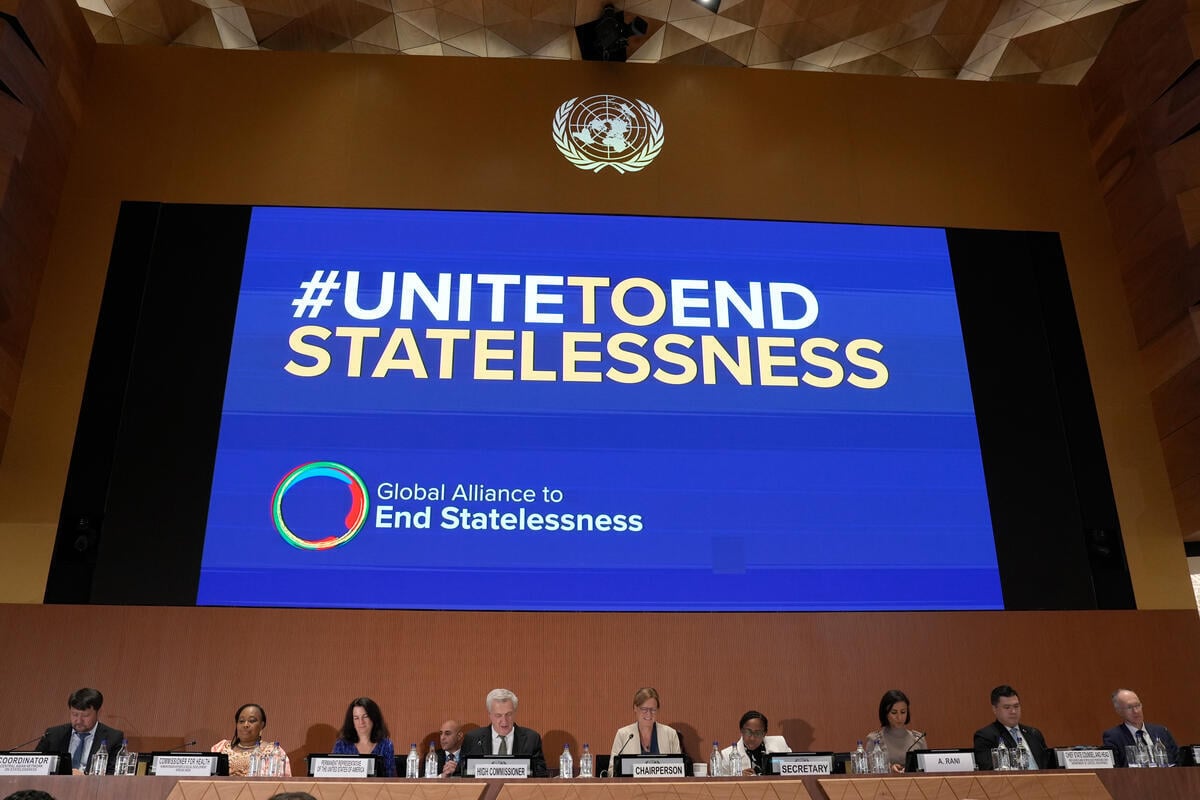 En una gran pantalla, por encima de un panel de personas sentadas, se lee en inglés UNIDOS PARA PONER FIN A LA APATRIDIA. Después: Alianza Global para poner fin a la apatridia