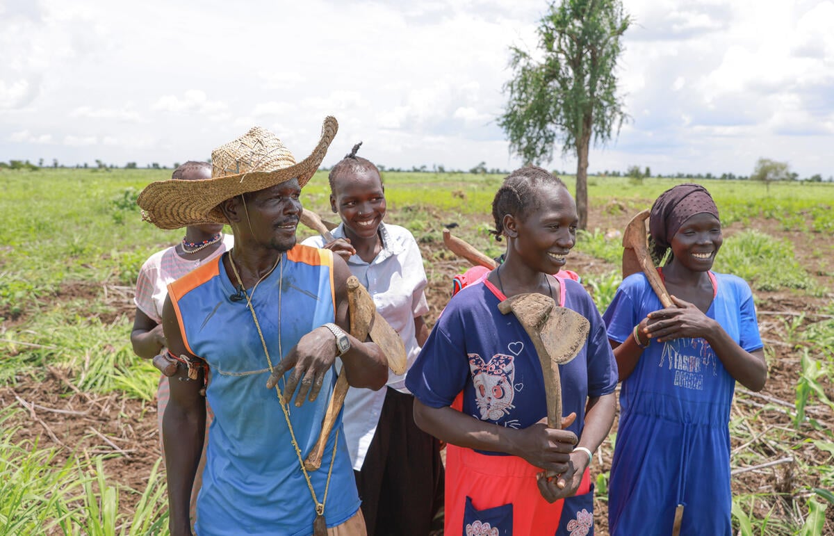 Un hombre, una mujer y tres jóvenes caminan por un campo sonriendo y sosteniendo herramientas de cultivo