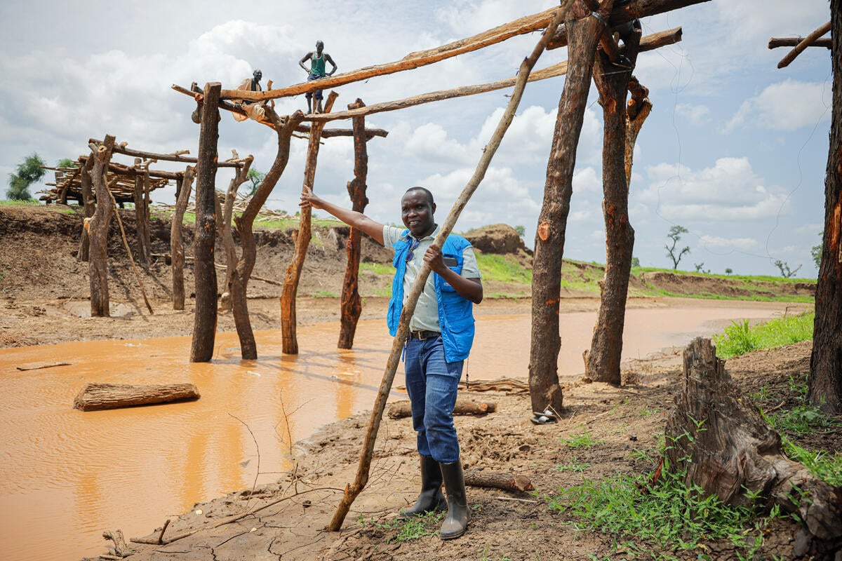 Un hombre con chaleco azul de ACNUR bajo un puente que se está construyendo sobre un río