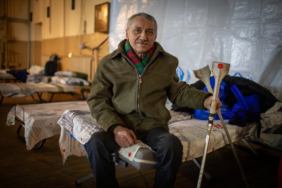 Sentado en una cama en un centro de tránsito, un hombre ucraniano de 59 años mira fijamente a la cámara; con la mano izquierda sostiene un par de muletas.