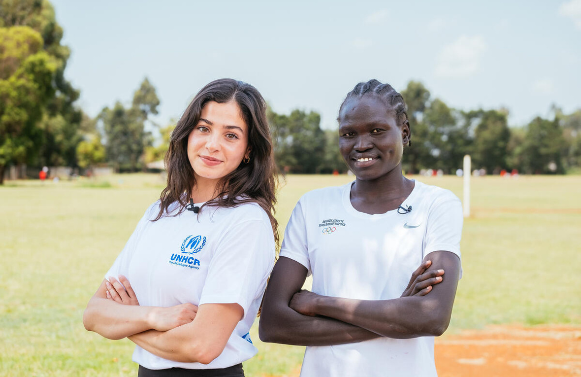 Dos mujeres de brazos cruzados con camisetas blancas de las olimpiadas, posan para la foto en un campo verde