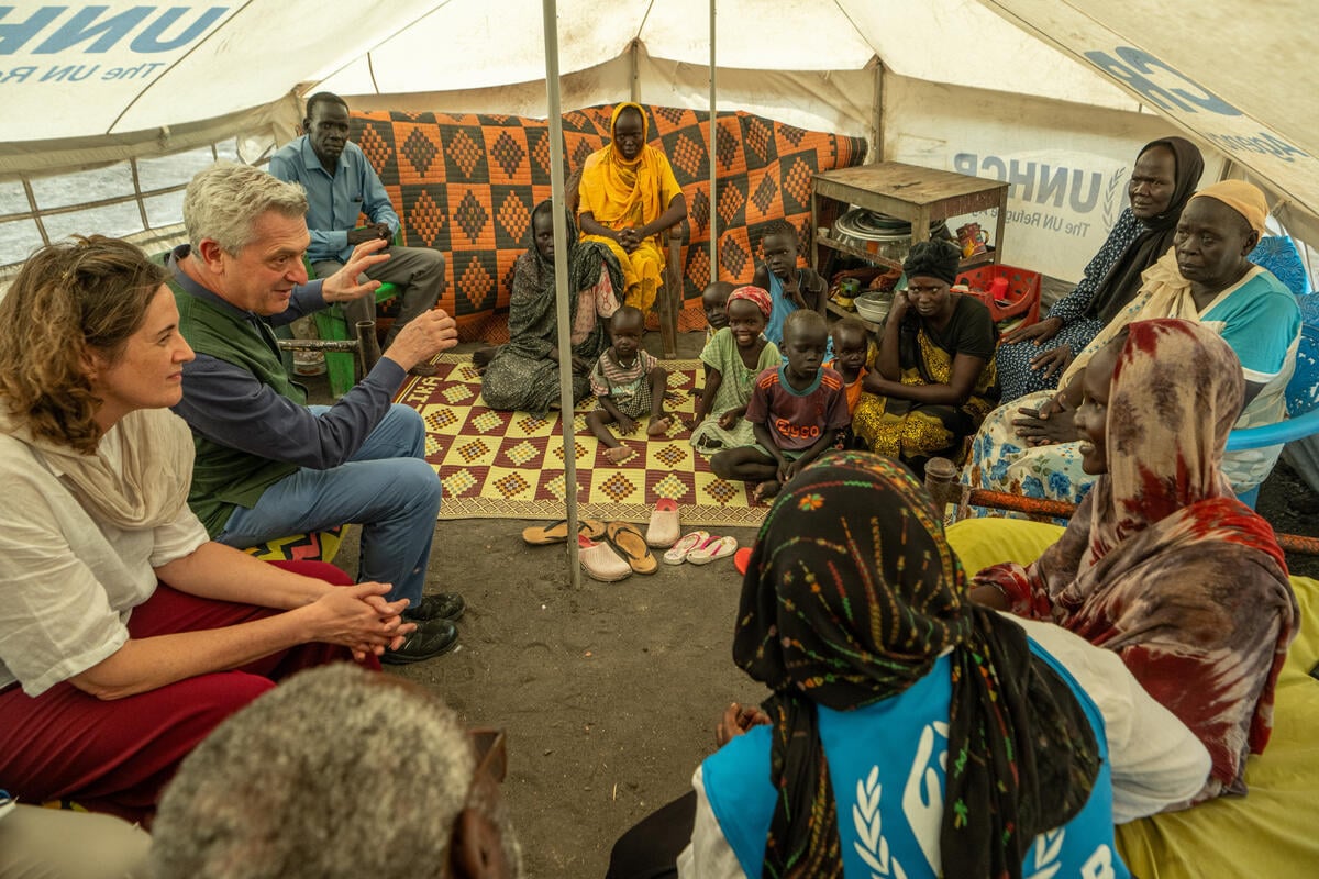 Dos trabajadores de ACNUR (uno de ellos es el Alto Comisionado, un hombre cano) charla con una familia sudsudanesa en un campamento de refugiados