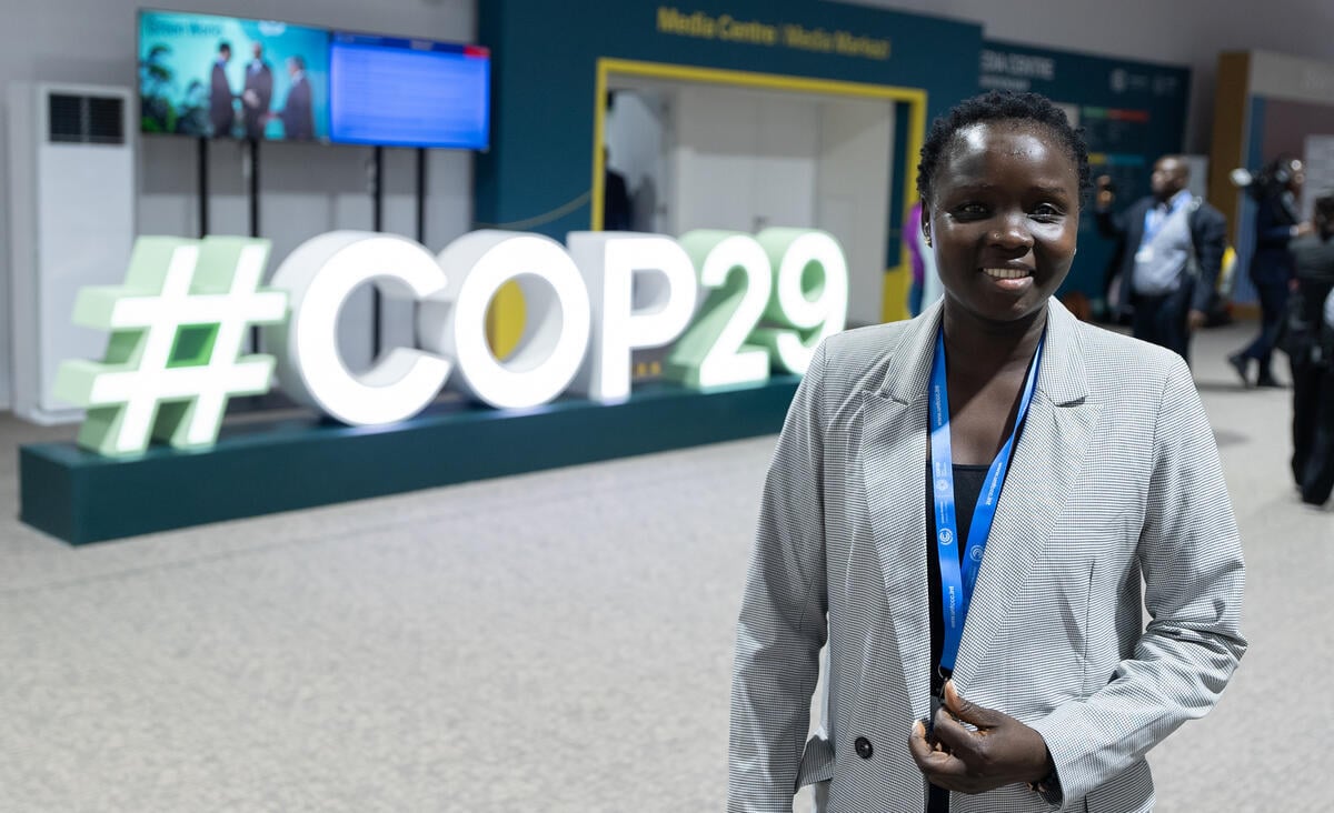 Una mujer frente que viste blazer gris frente a grandes letras blancas que dicen #COP29