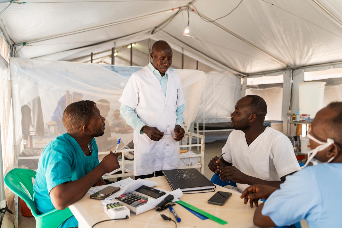 Cuatro médicos sudaneses – todos hombres – conversando alrededor de una mesa circular. Uno de ellos está de pie.