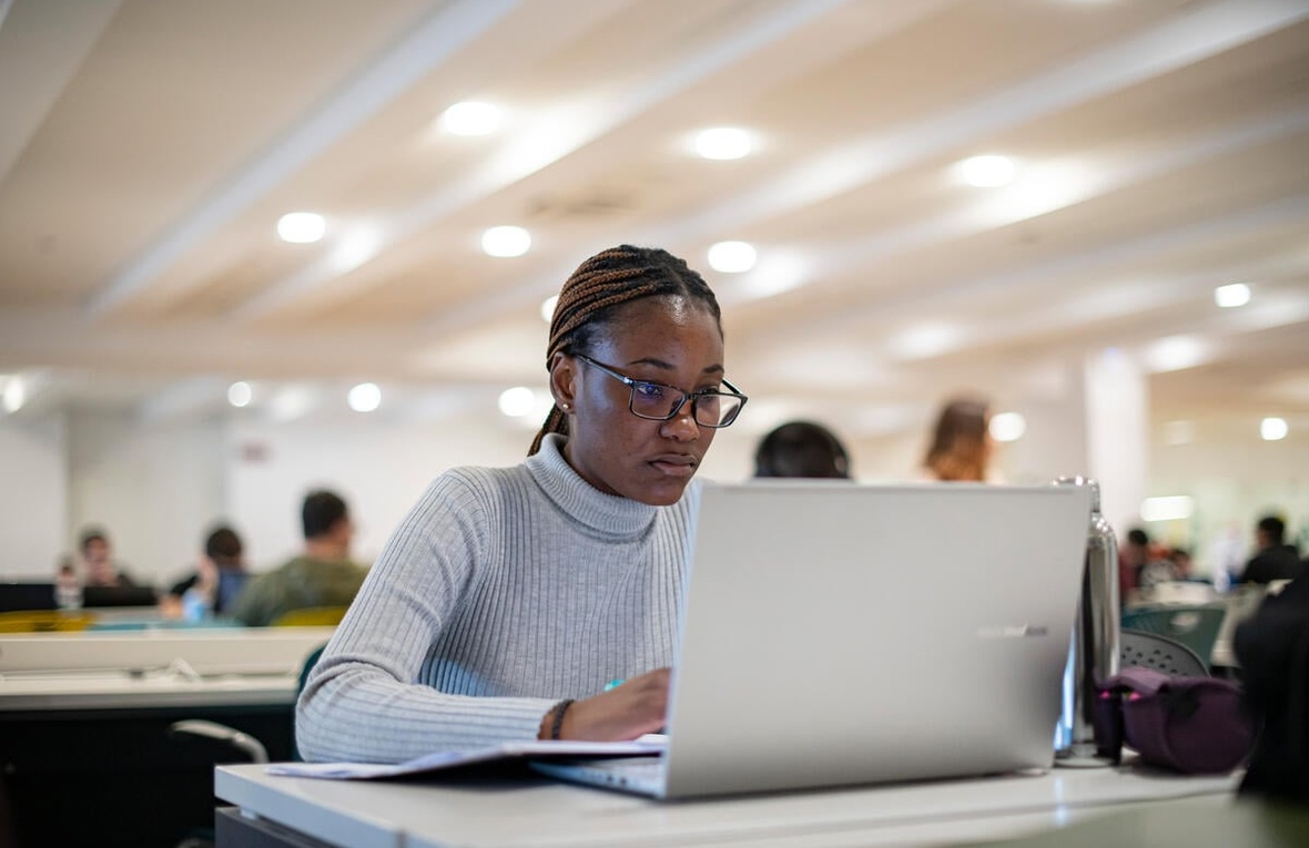 Una estudiante en su computadora portátil en una biblioteca universitaria