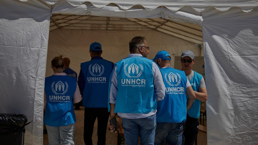 Un grupo de personas que llevan puesto un chaleco azul con el logotipo de ACNUR ingresa a una carpa