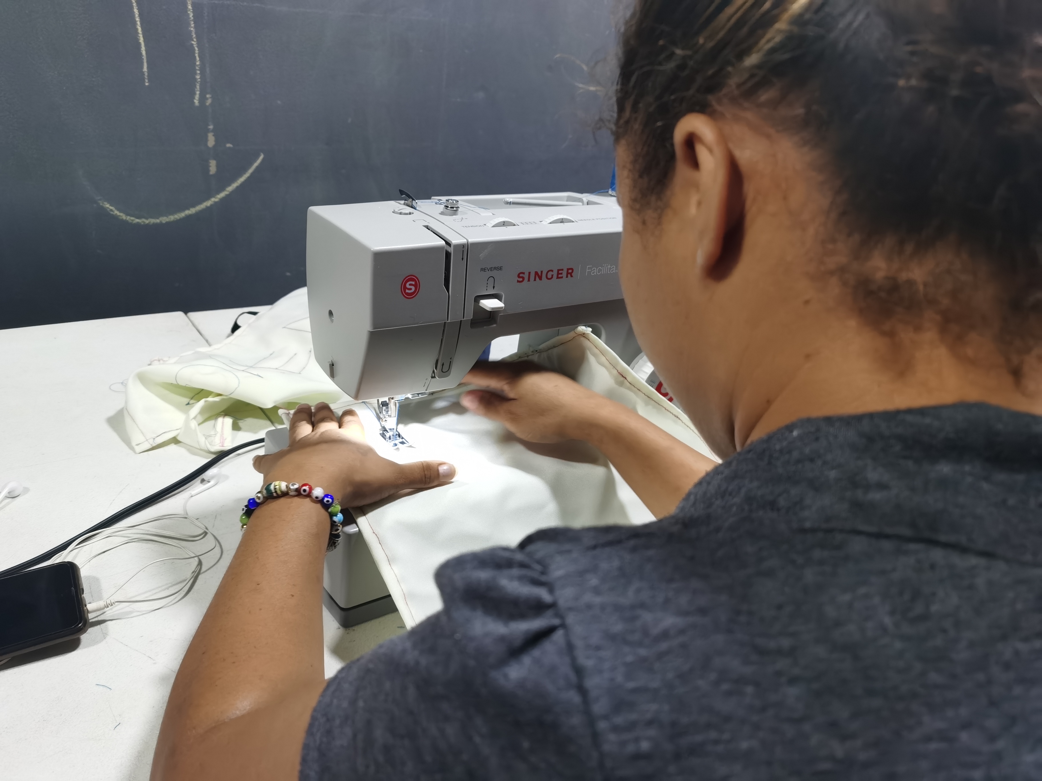 Foto de espaldas a una mujer con camiseta gris oscuro que utiliza una máquina de coser