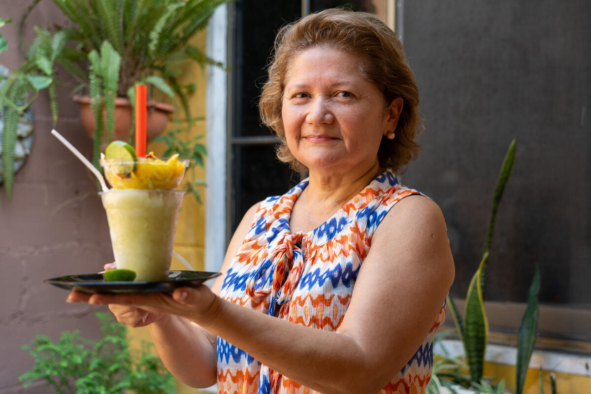 Una mujer sostiene con ambas manos una bandeja con una bebida decorada con frutas.