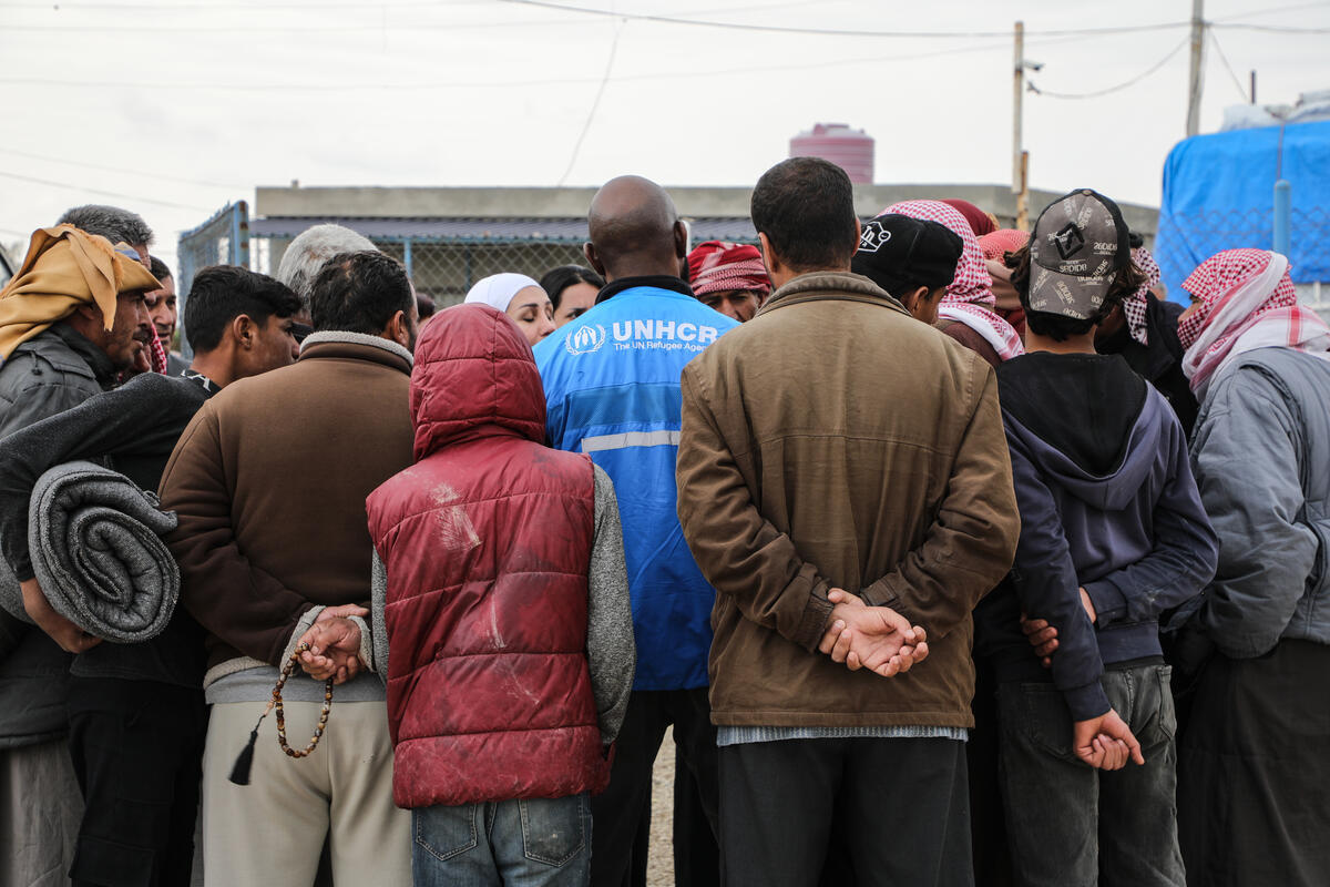 Un grupo de personas reunidas en torno a un trabajador de ACNUR; todas le dan la espalda a la cámara.