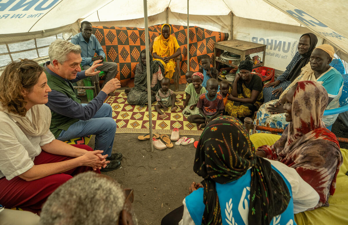 Dos trabajadores de ACNUR (uno de ellos es el Alto Comisionado, un hombre cano) charla con una familia sudsudanesa en un campamento de refugiados