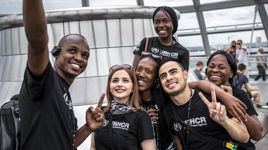 Un grupo de personas jóvenes, que llevan playeras de ACNUR, se toman una selfi.