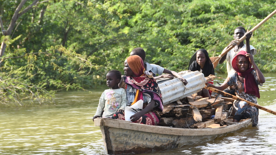 Varios adultos y niños viajan en una canoa apilada con madera y hierro ondulado.