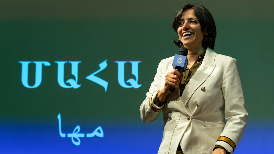 Una mujer de cabello corto oscuro, sostiene un micrófono con logotipo de ACNUR